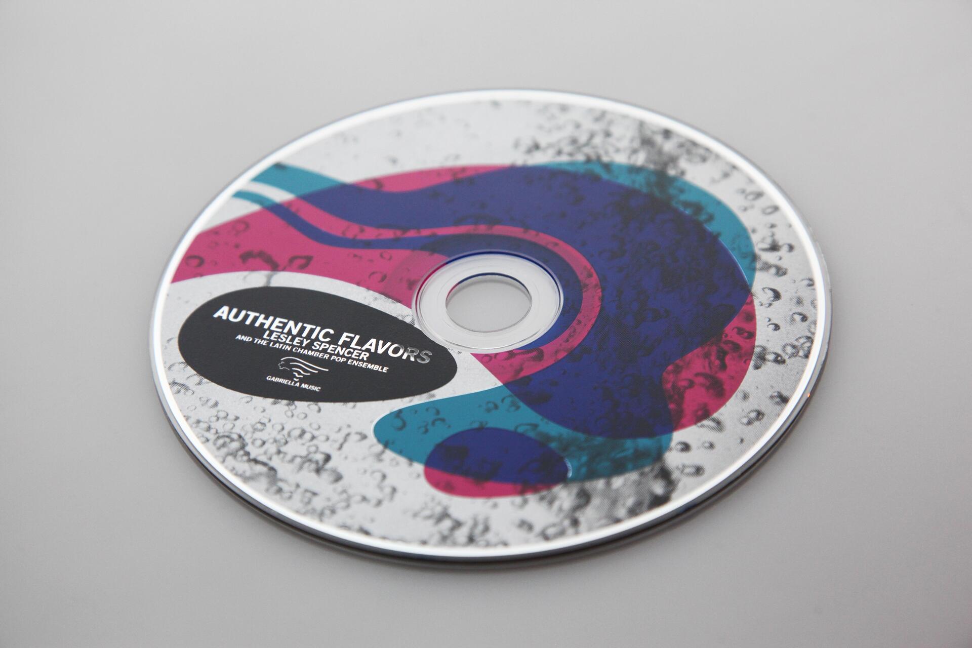 CD with colorful abstract design and text: "Authentic Flavors, Lesley Spencer and The Latin Chamber Pop Ensemble." Circular droplets adorn the surface.