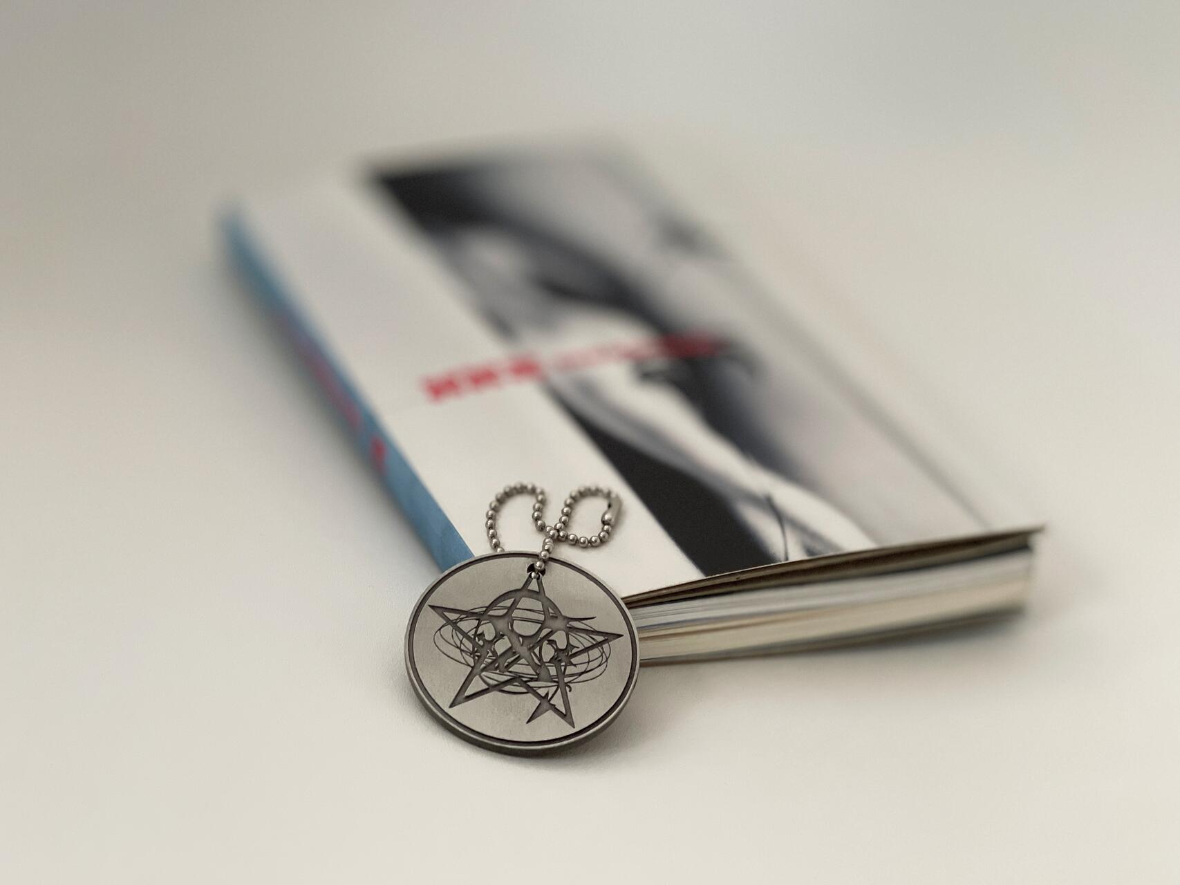 Metal pendant with an intricate design on a beaded chain, placed on top of a closed book with a blurred cover.