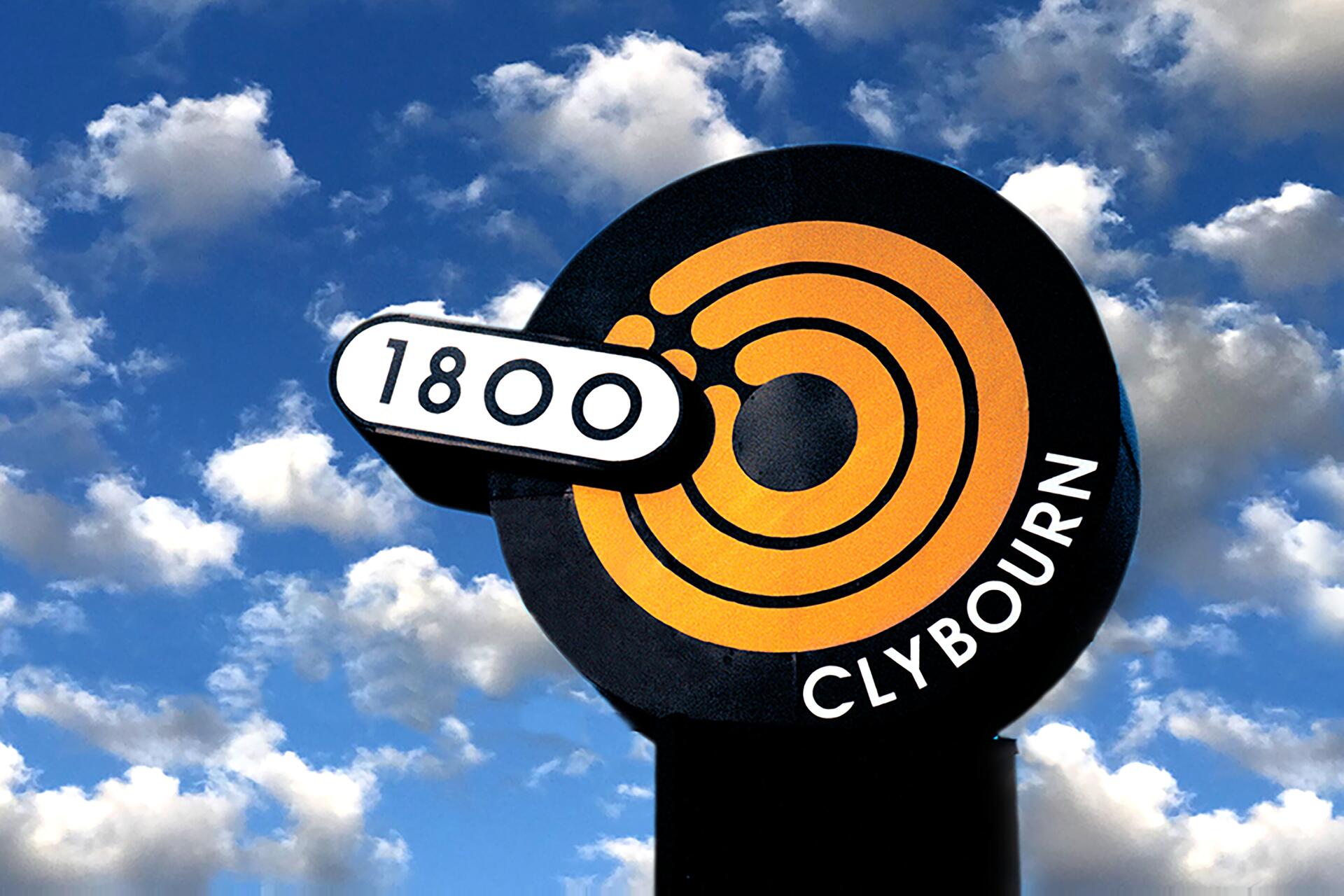 Sign with concentric orange circles and text "CLYBOURN" below, next to "1800" in a white oval. Background shows a cloudy blue sky.