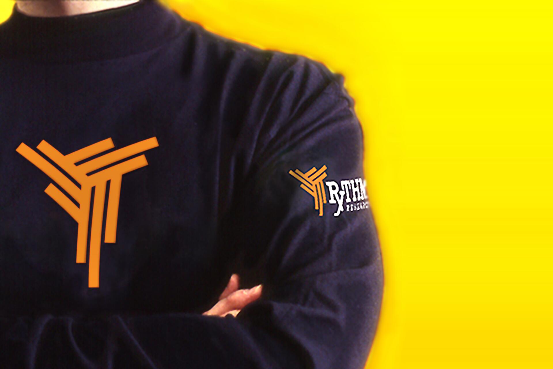 Man in dark sweater with orange abstract logo on chest, yellow background.