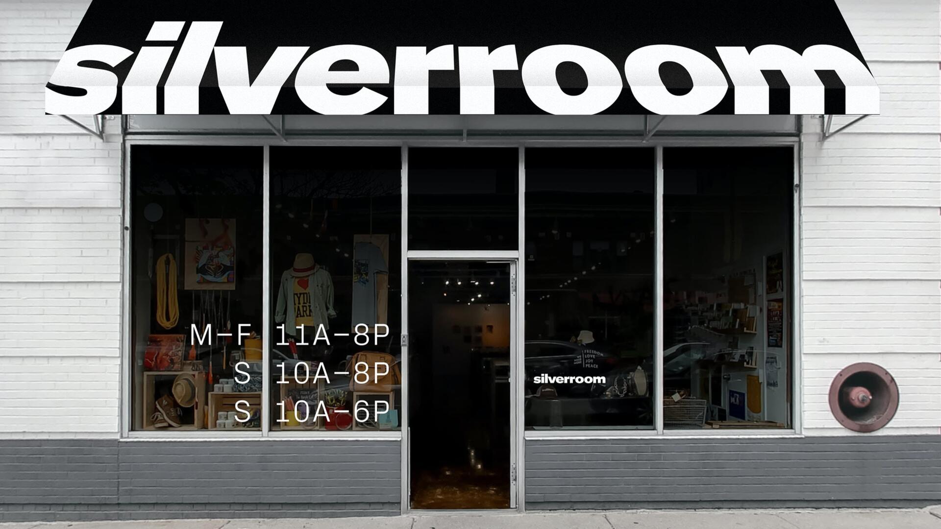 Storefront of "Silverroom" with a black awning displaying the name in bold white letters, large glass doors and windows showing clothing and other items inside. White building with a brick-gray base.