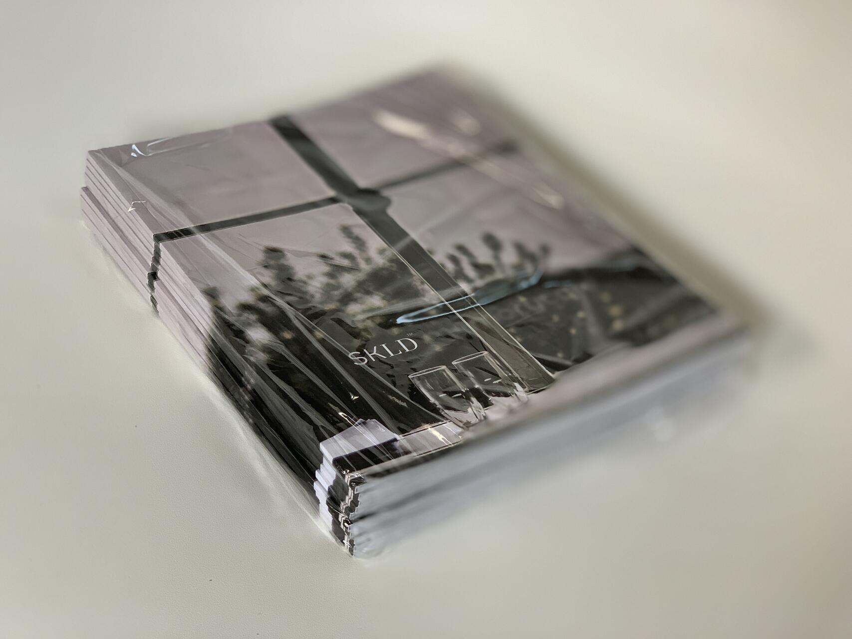 Stack of sealed magazines with a cover image showing an outdoor scene, placed on a light-colored surface.