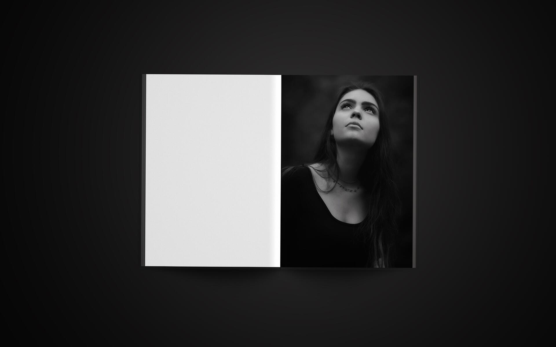 Open book on a dark surface, with a black and white photograph of a woman looking upwards on the right page. The left page is blank.