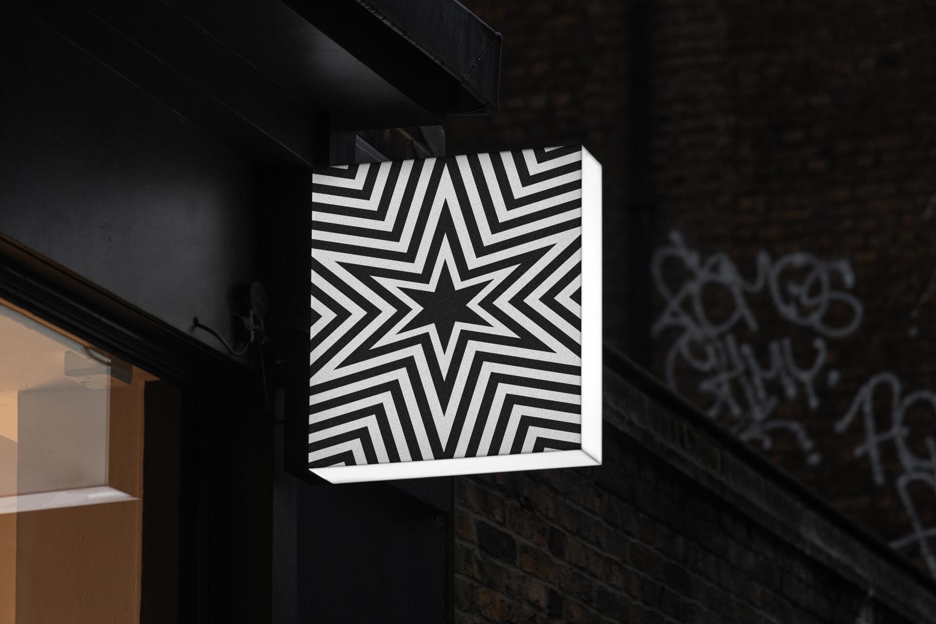 Black and white sign with a geometric star pattern, mounted on a dark building facade. Graffiti visible in the background.