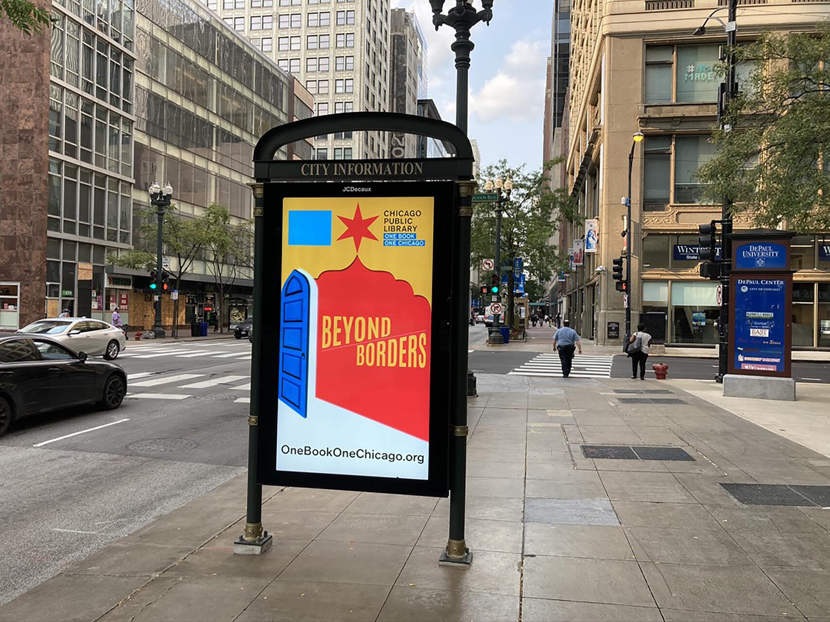 A colorful poster displayed on a city street board with the theme "Beyond Borders," featuring abstract designs in red, yellow, and blue. People are walking in the background on a busy urban sidewalk with tall buildings and parked cars.