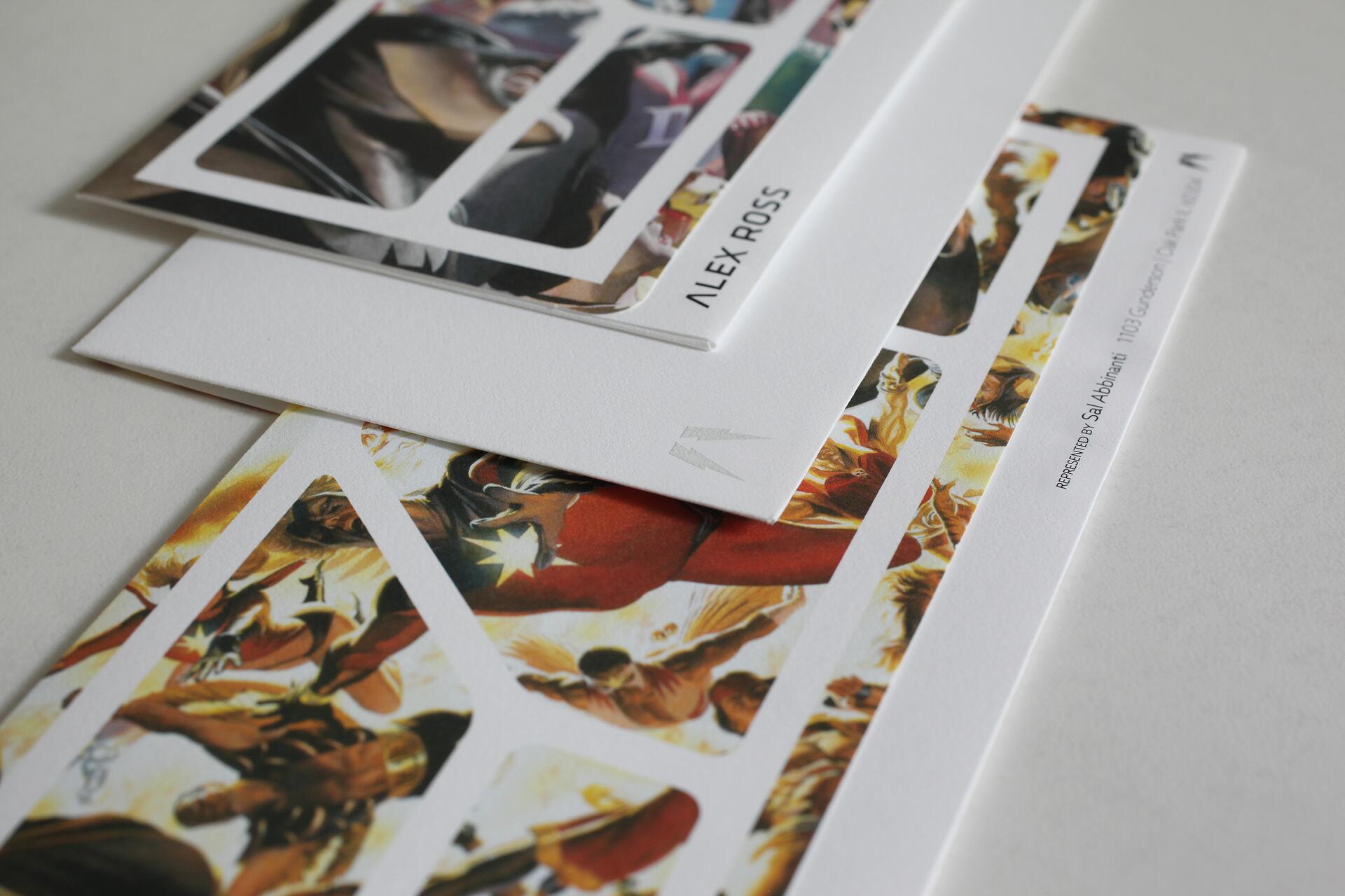 Stacked art prints featuring dynamic and colorful comic-style illustrations, with the text "ALEX ROSS" partially visible.