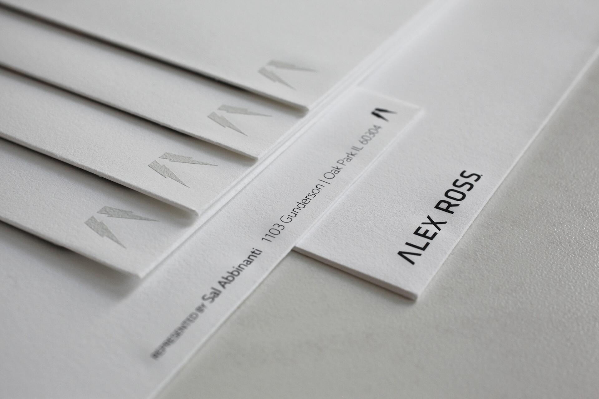 Business cards fanned out with embossed lightning bolt logos and the name "Alex Ross" in bold black text on one card. The cards have a clean, minimalist design.