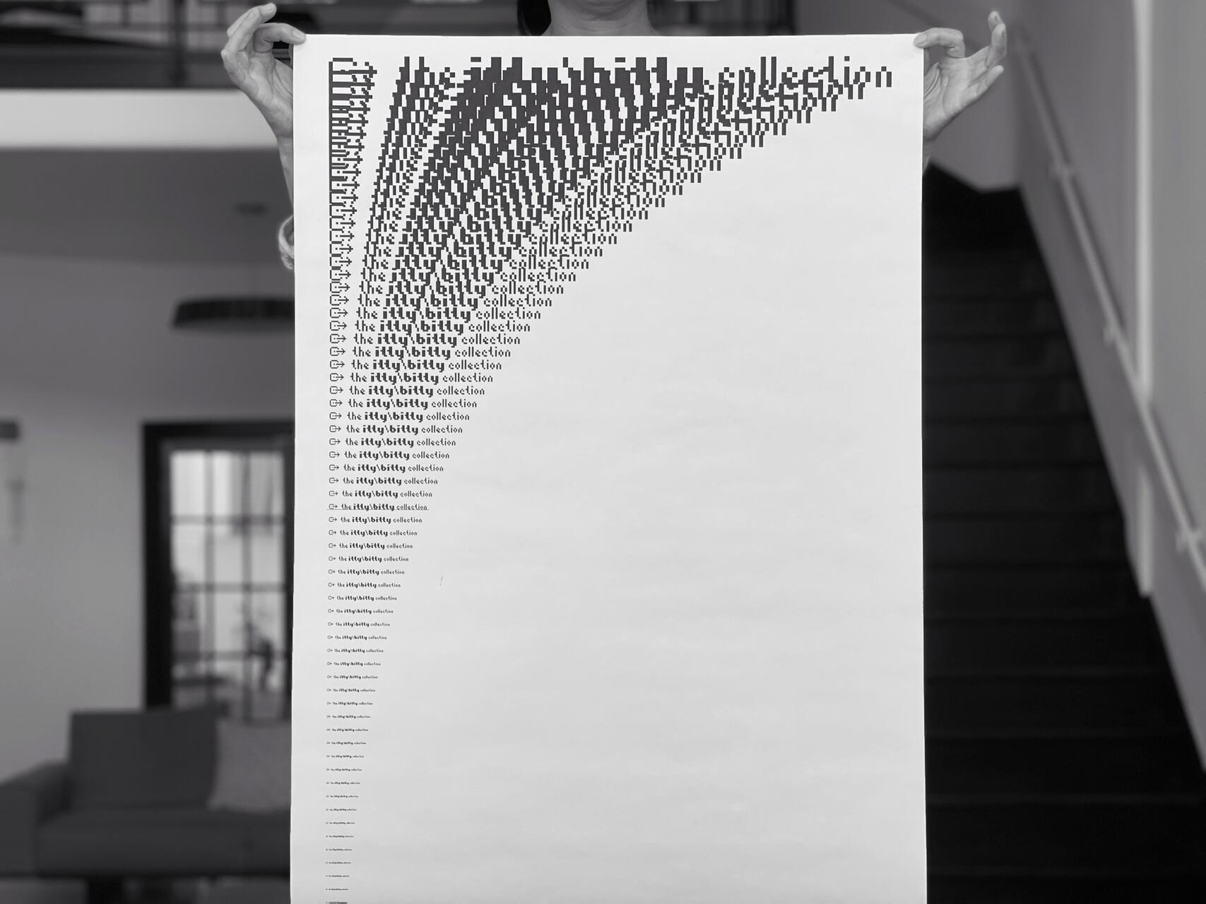 A person holds a large poster with a series of progressively smaller, repeating text patterns in black on a white background, set in a modern interior with a staircase and furniture.