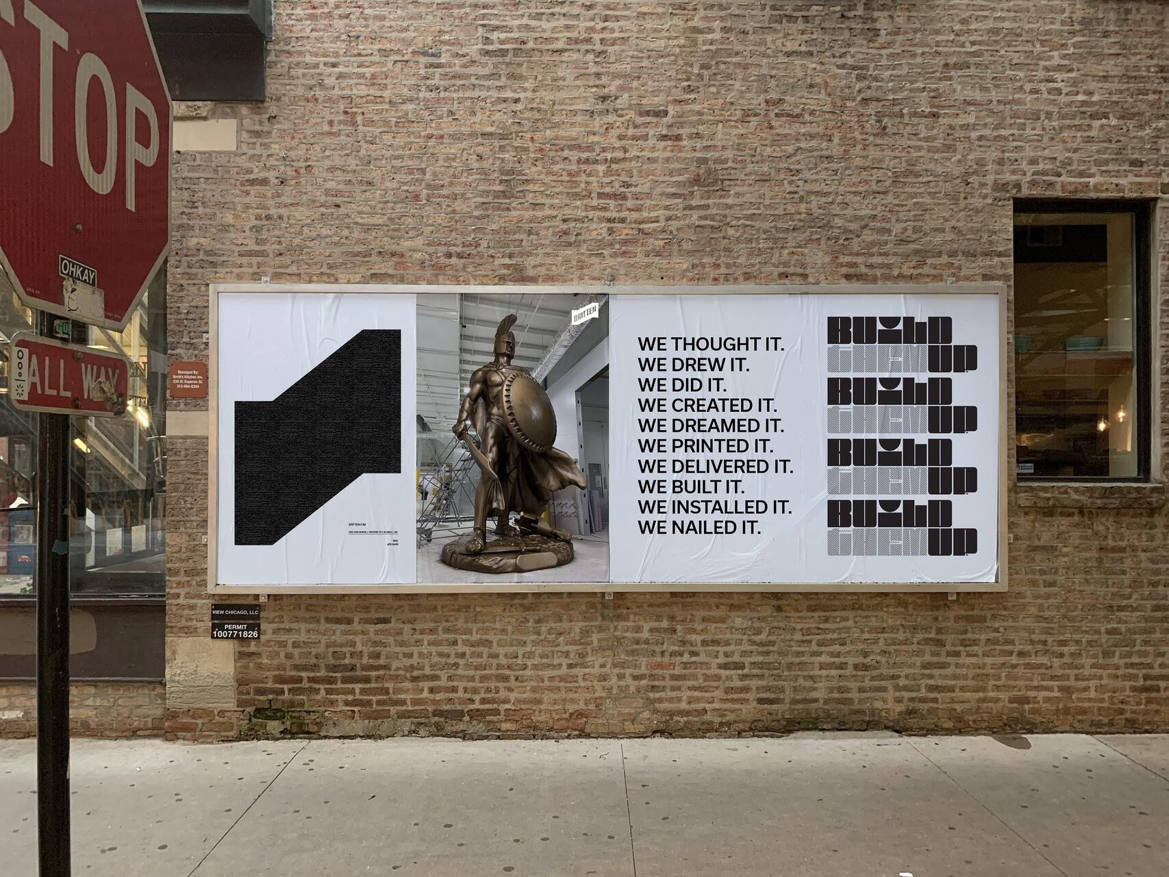 Billboard on a brick wall featuring an abstract black shape, a bronze warrior statue, and text on a white background. The text repeats phrases about creativity and construction. A stop sign is visible to the left.