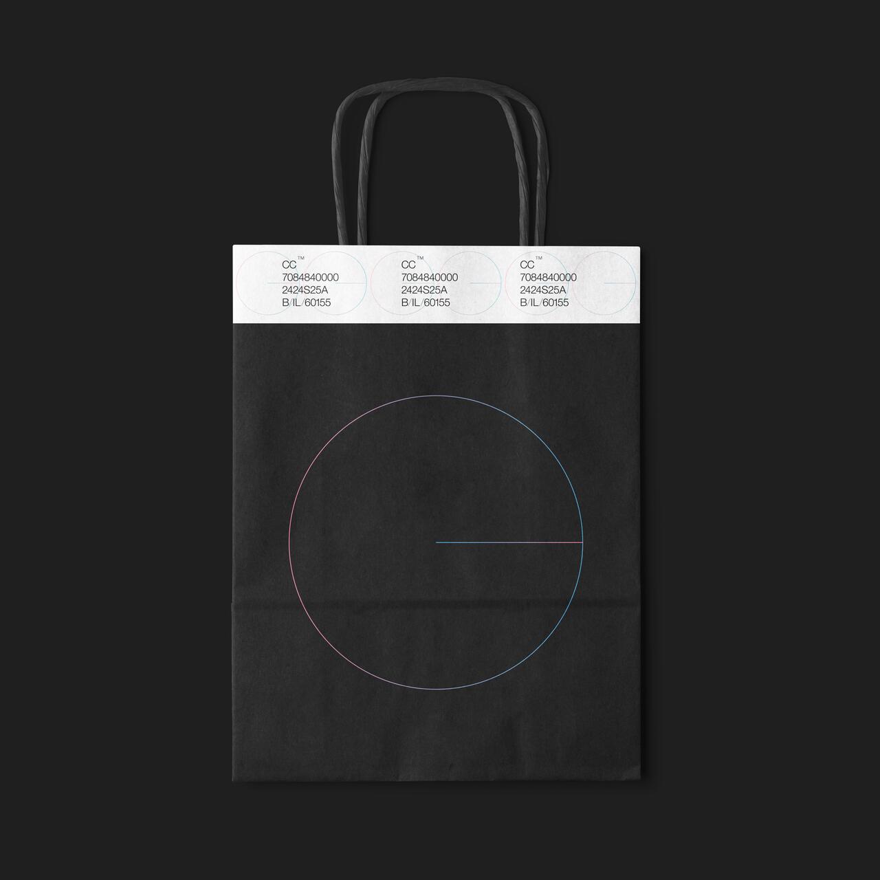 A black shopping bag with thin handles, featuring a simple geometric design of a colored circle and line. Top part displays a strip with printed text and numbers.