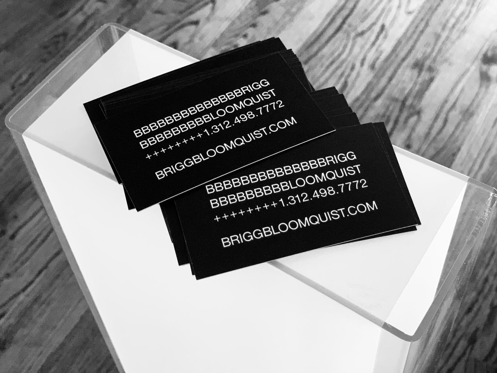 Black business cards with white text stacked on a white surface with a wooden floor background.