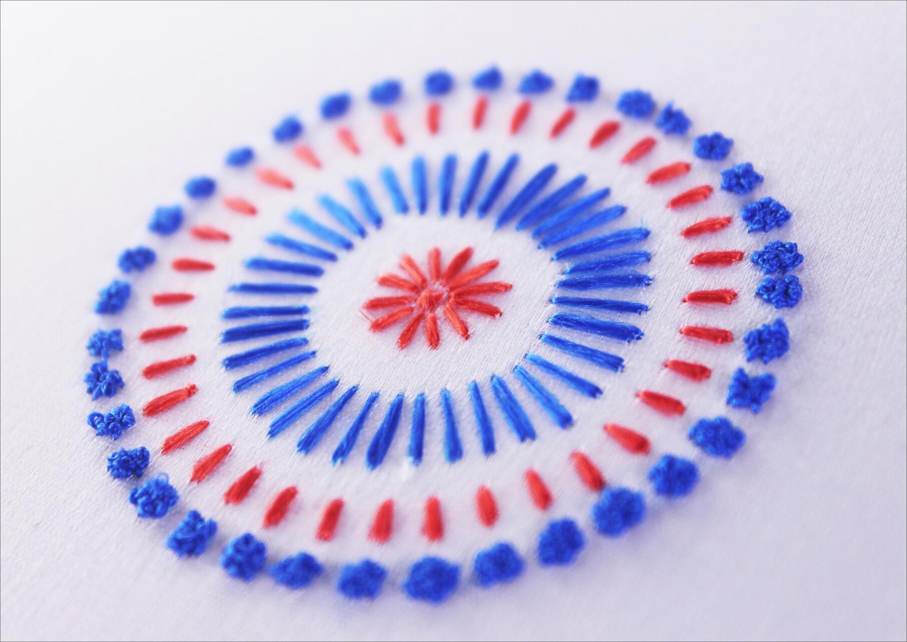 Circular embroidery pattern with blue and red threads on white fabric.