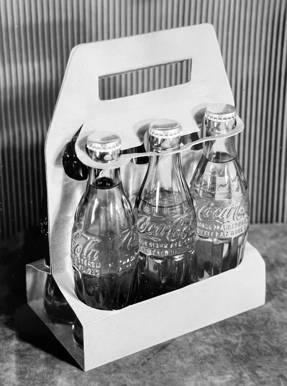 Six vintage glass soda bottles in a cardboard carrier with a handle.
