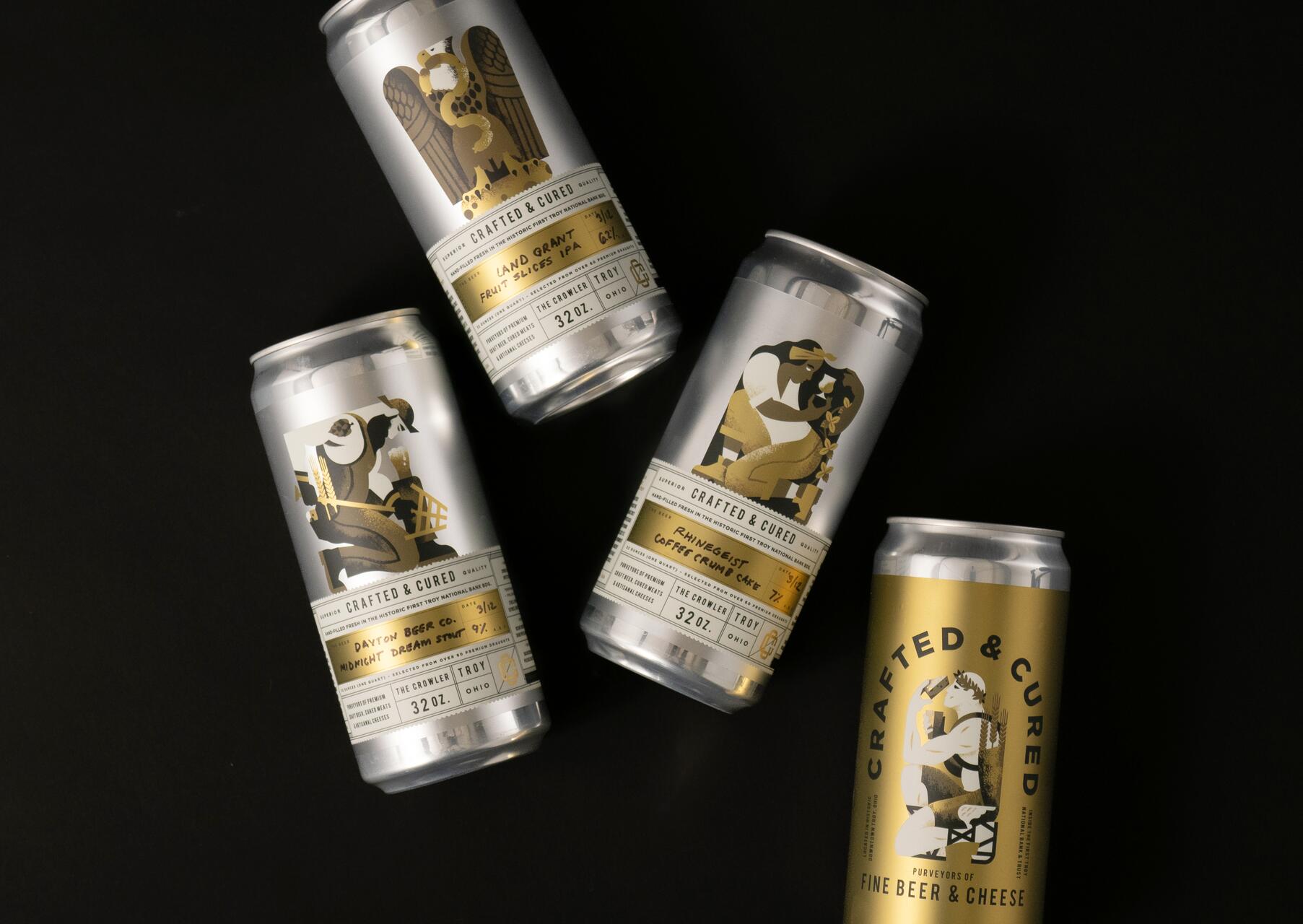 Four silver cans with artistic gold designs and labels on a black background, featuring different beer names and artwork. One can is gold.