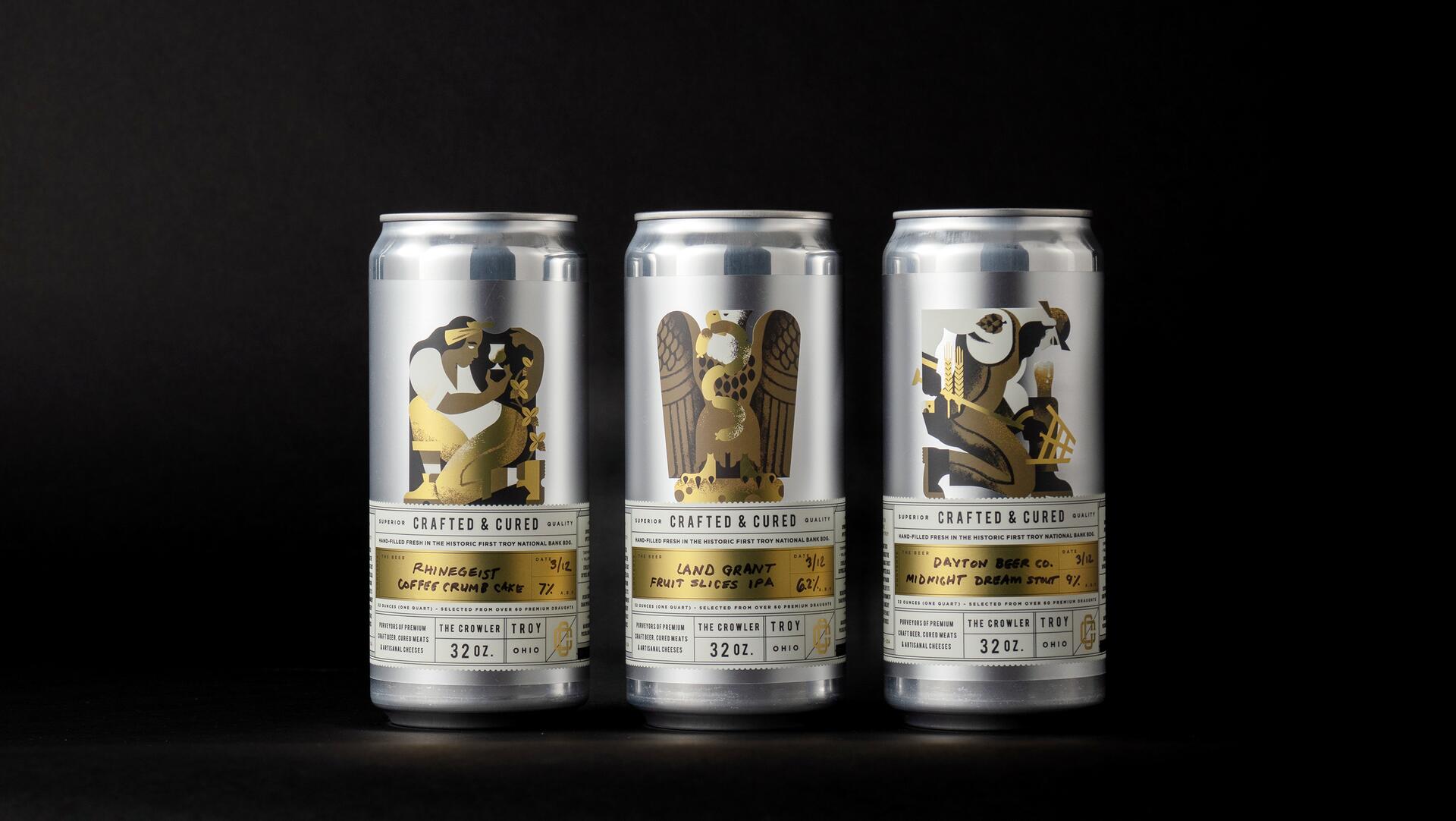 Three silver beverage cans with artistic gold labels featuring unique illustrations on a black background.