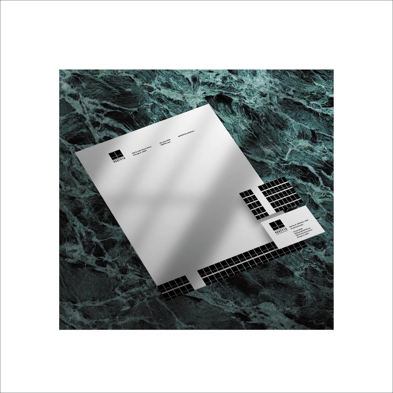 White stationery with black grid designs, including a letterhead and business card, lies on a textured green marble surface.