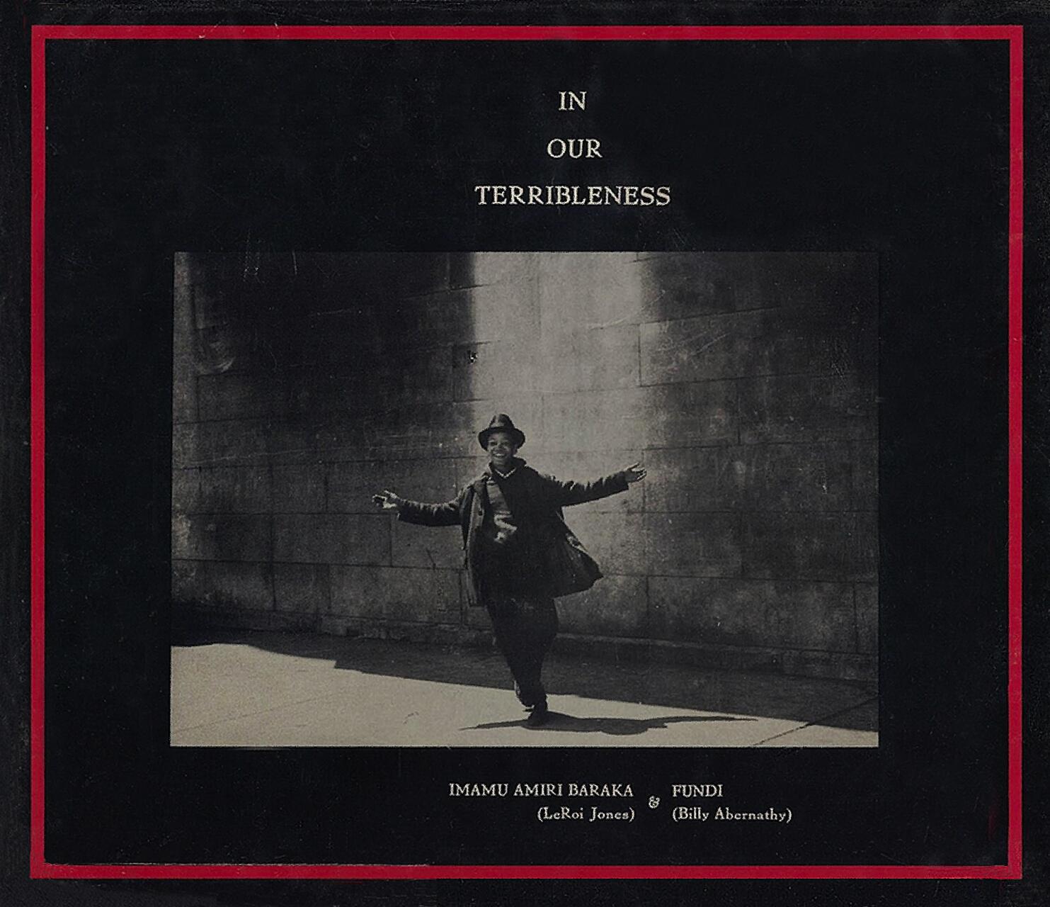 A black and white photograph of a person joyfully extending their arms while walking in front of a stone wall, wearing a hat and coat. The image is centered within a black border with red lines, and text above and below the photograph.