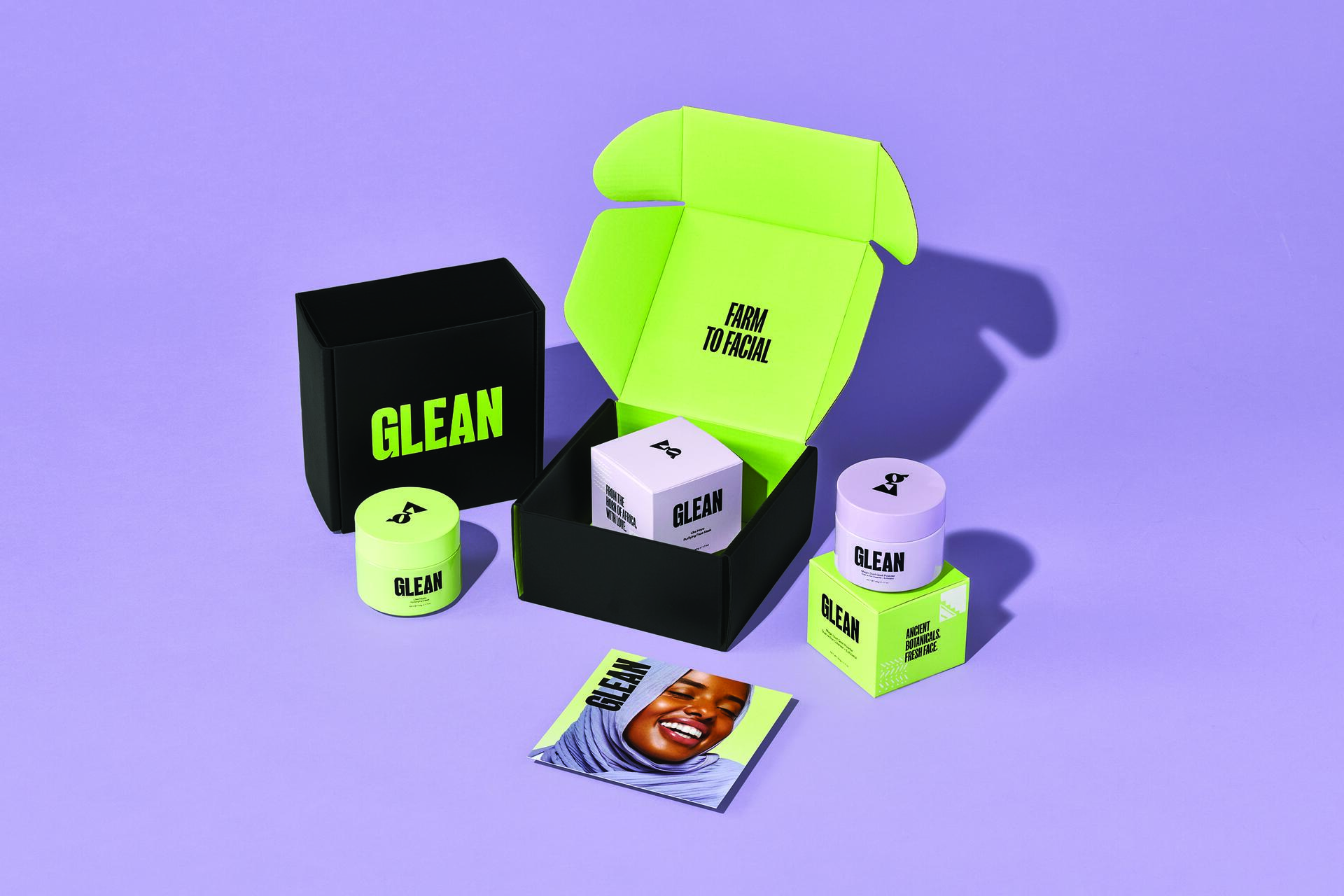Skincare product display on a purple background. Black and neon green packaging from "Glean," including jars and an open box with "Farm to Facial" inside. A brochure with a smiling person’s face lies nearby.