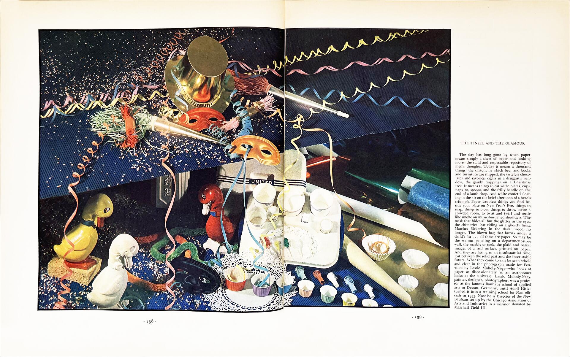 26A-10_Moholy-Nagy Double Page Ad: Table covered with festive items, including colorful streamers, confetti, hats, and small toys like ducks. A tray holds cups, while rolls of paper and a golden mask add to the celebratory theme. On the right is a block of text.