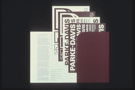 Folder with white papers displaying "PARKE-DAVIS" in bold text and a logo. The papers are partially covered by a maroon sheet, arranged neatly on a dark background.