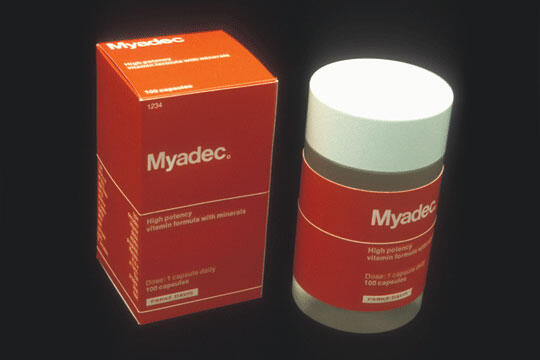 Red and white Myadec vitamin packaging with a box on the left and a bottle on the right against a dark background.