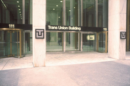 Entrance of the Trans Union Building with large glass doors, flanked by two revolving doors. The facade features a sign with the building's name and the numbers 111 and 115.