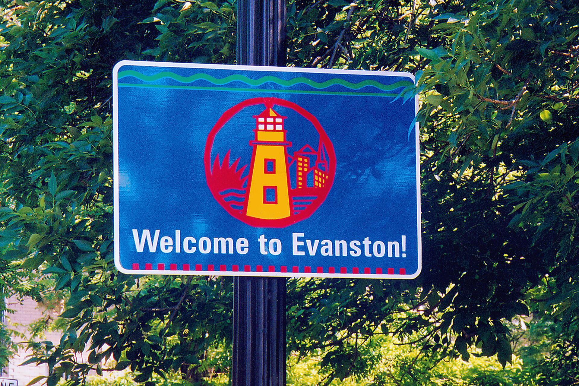 Blue welcome sign with a lighthouse and city graphic, surrounded by trees.