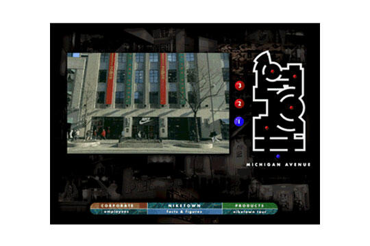 Photograph of a modern building with large windows and multicolored vertical banners. A sidewalk with pedestrians passes by. Adjacent is a stylized map labeled Michigan Avenue, with numbered markers in red and blue.