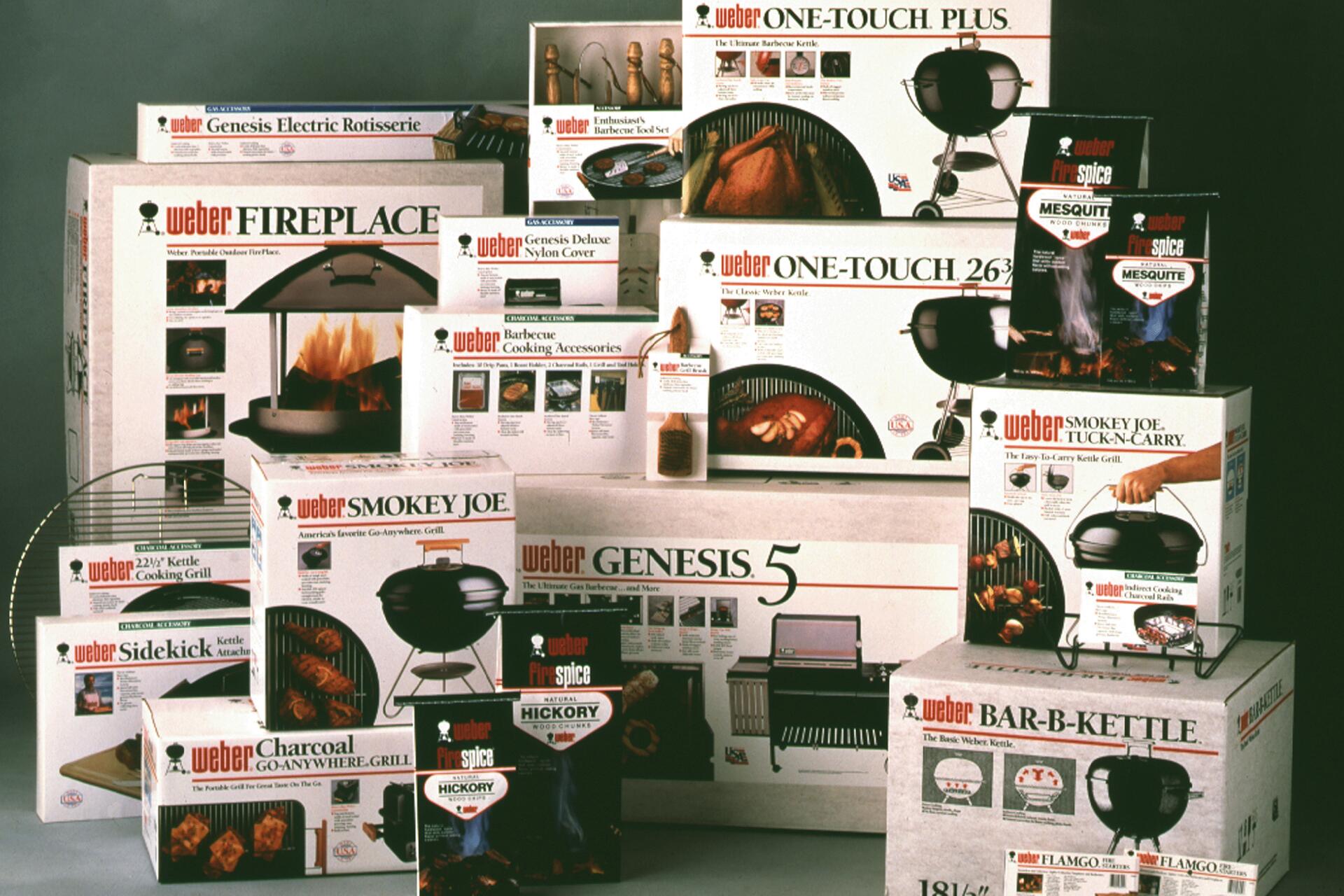 Various Weber barbecue product packages, including grills, accessories, and seasoning sets, are stacked together. The boxes feature images of barbecue items like grills and spice packets, and are predominantly white with red and black text.