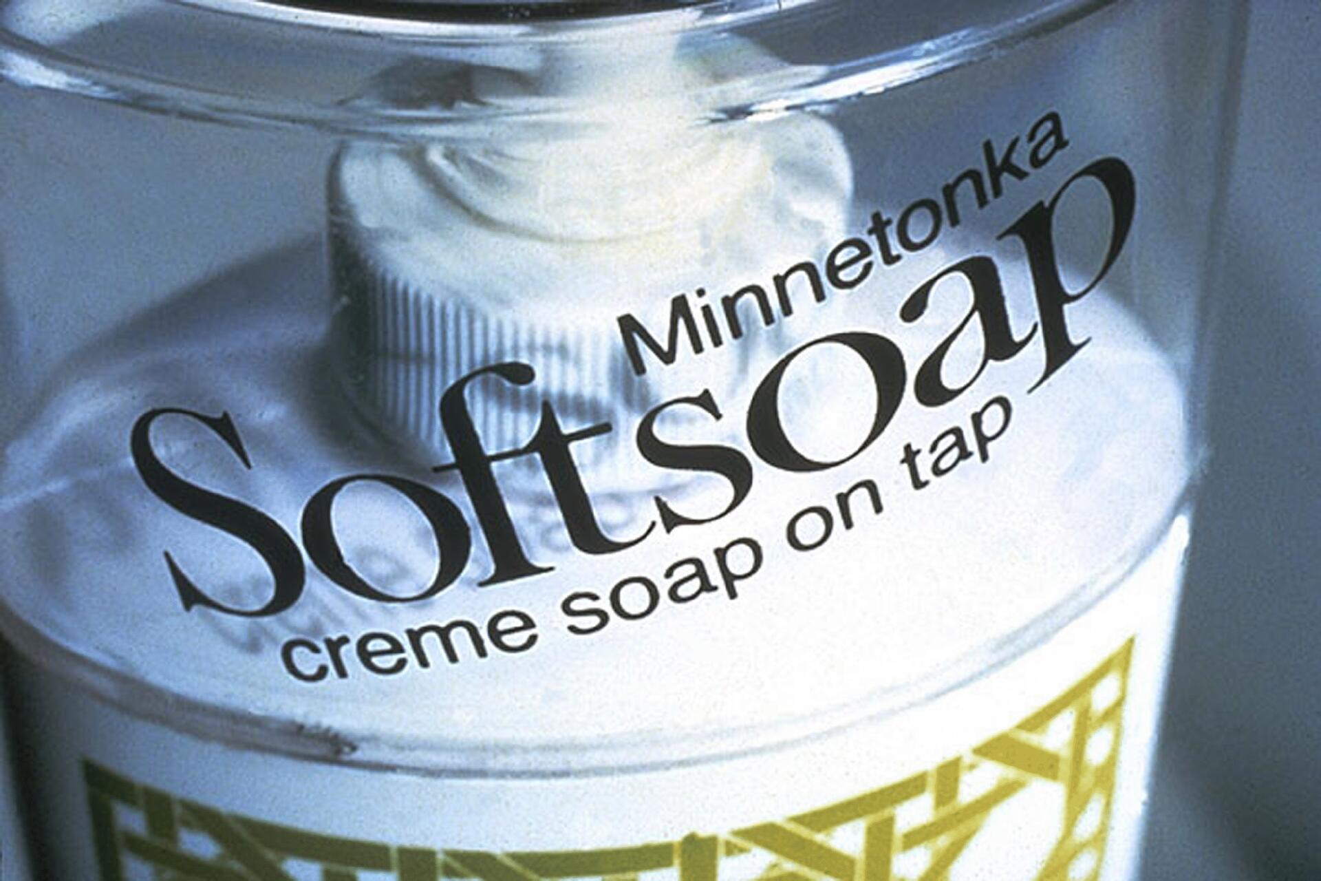 Close-up of a Softsoap dispenser with a visible pump, labeled "Minnetonka Softsoap creme soap on tap." The container is clear, revealing a white and patterned design inside.
