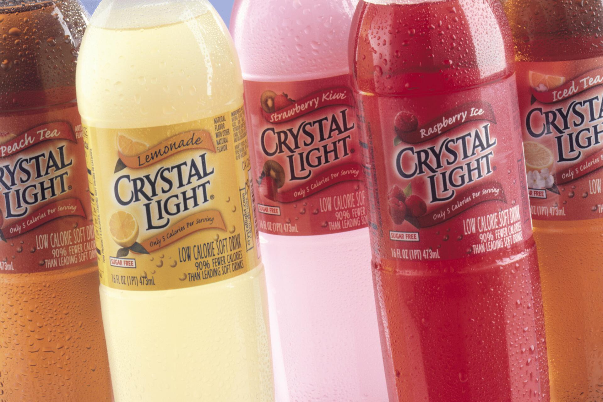 Colorful bottles of Crystal Light drinks with labels displaying flavors like lemonade, strawberry kiwi, and raspberry ice. Each bottle features vibrant colors and condensation droplets, suggesting freshness.