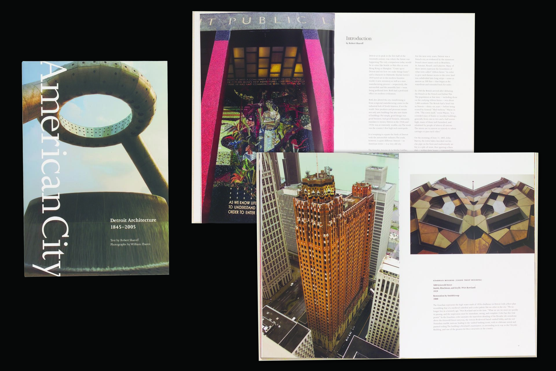 Books with photographs of Detroit architecture, featuring a cover with a circular sculpture in front of a skyscraper. Inside, pages display images of a colorful mosaic and an aerial view of a tall, brown building with geometric designs.
