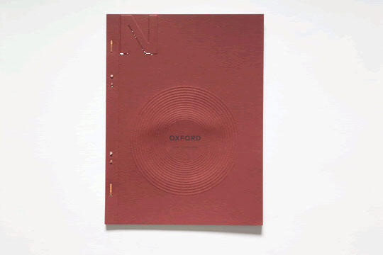 Red notebook with embossed concentric circles and the word "Oxford" in the center. The cover has a minimalist design with a sleek texture.