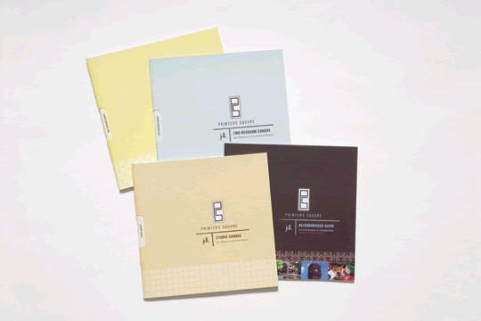 Four square brochures arranged in a fan shape, featuring different colors: two yellow, one light blue, and one dark brown. Each brochure displays text and a logo on the front cover.