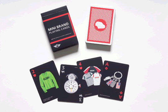 Mini brand playing cards on a white surface. An open box reveals four cards: two of hearts with a green sweater, three of hearts with a watch, four of hearts with shirts, and ace of hearts with keychains. A deck is partially visible.
