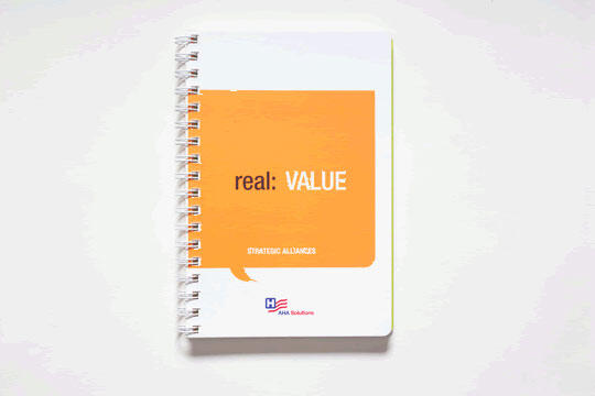 Spiral-bound notebook with a white cover featuring an orange speech bubble. Text inside the bubble reads "real: VALUE," with "STRATEGIC ALLIANCES" beneath. A small logo and the words "HA Solutions" are at the bottom.