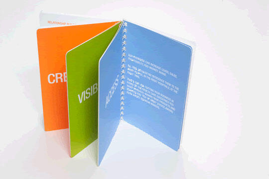 Three colorful pages in a standing open booklet: orange, green, and blue, each with bold white text partially visible. Pages appear to be connected by a spiral binding, set against a white background.