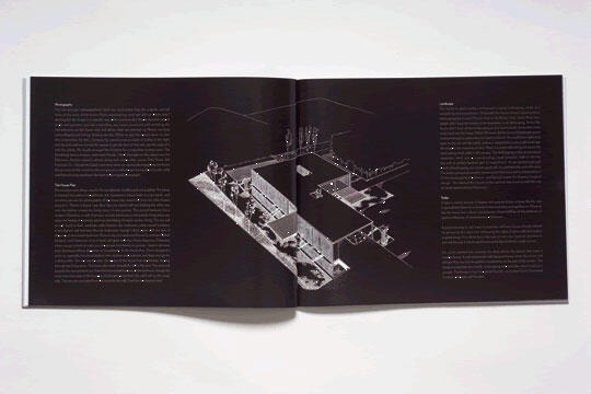 An open magazine showing a black and white architectural rendering of a modern building centered on a dark background, with columns of text on both pages.