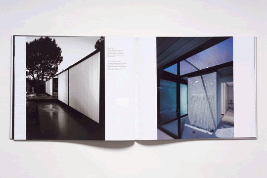 Open book showing architectural photographs of modern buildings. One page features a black and white image of a structure with trees, and the other displays a color photo of a glass-walled room with reflections. Both are minimalist designs.