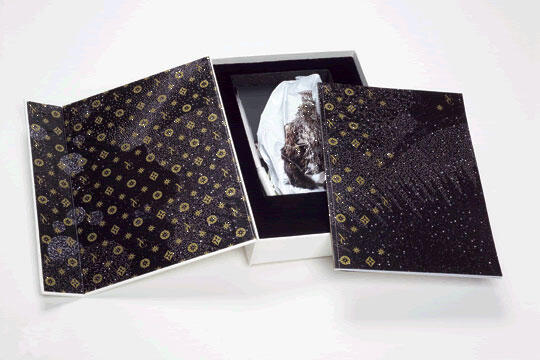 Decorative box with a black and gold pattern, open to reveal an intricately wrapped item inside.