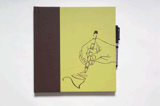 Notebook with a yellow cover featuring an illustration of a hand holding a pen, writing a squiggly line. The notebook's spine is brown, and a black pen is clipped to the right edge.