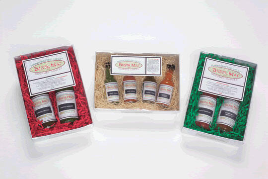Three neatly arranged gift boxes with jars of sauces. The left box is lined with red shredded paper, the middle with straw, and the right with green shredded paper. Each box has a different sauce label on top.