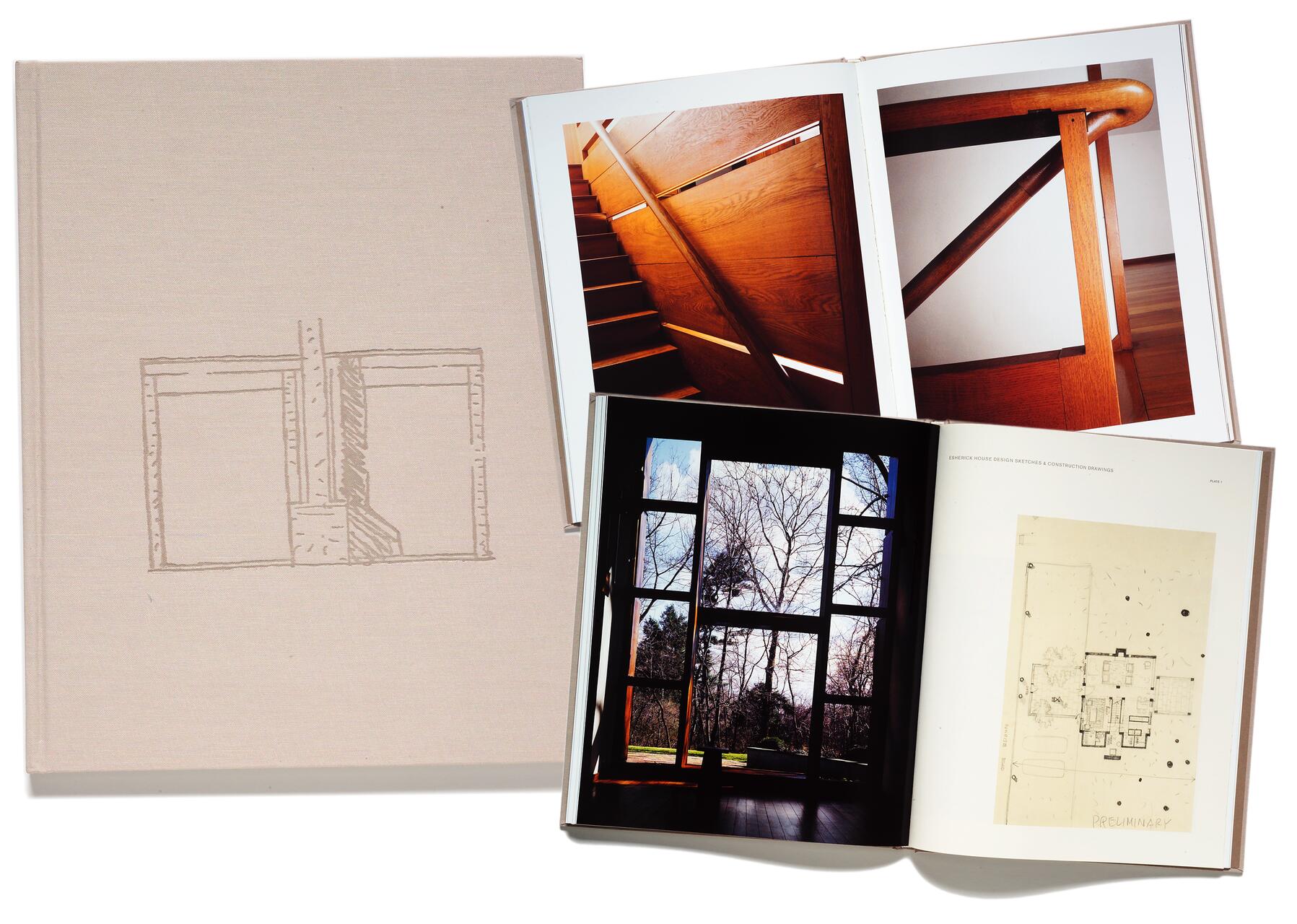 A beige hardcover book with a sketch on the cover is open, displaying pages with photographs of wooden architectural details, a large window view of trees, and an architectural blueprint.