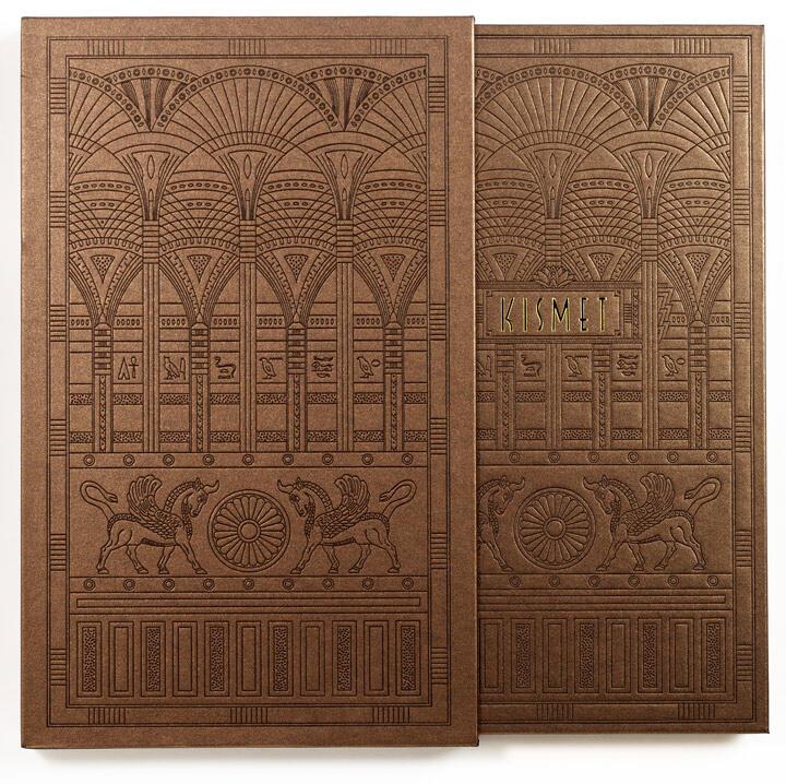 Ornate brown book cover with embossed designs of arches, mythical creatures, and a central floral motif. The word "KISMET" is embossed in gold on the right panel.