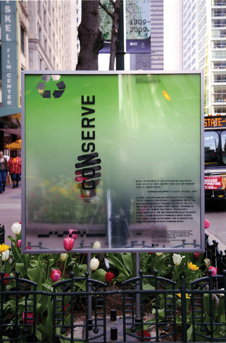 Sign with translucent green background and the word "CONSERVE" in vertical black text, featuring a recycling symbol. Surrounded by blooming tulips, it is located on a bustling city street with tall buildings in the background.