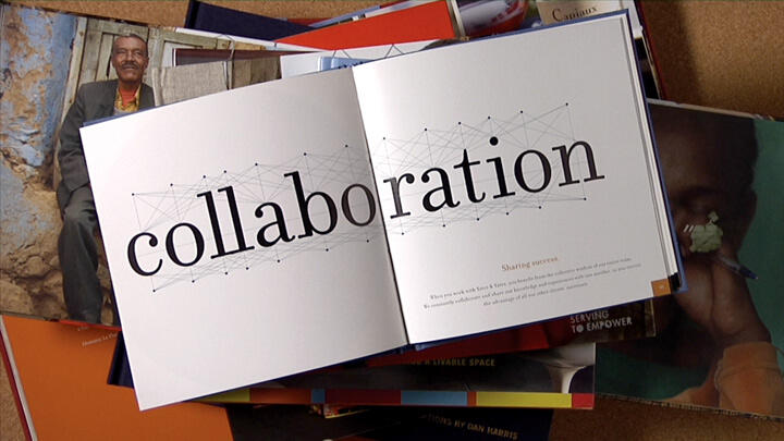 Open book displaying the word "collaboration" with a geometric design, placed on top of a stack of various colorful books.