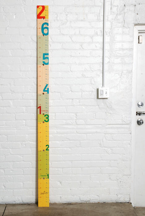 Colorful vertical growth chart with large numbers against a white brick wall next to a door.