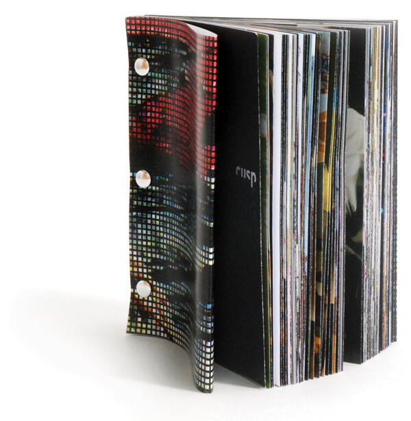 A thick booklet with a colorful, pixelated patterned cover fastened by four white rivets along the spine, with the word "cusp" visible on the front page.