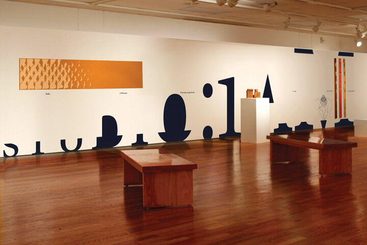 Art gallery with wooden benches and a white wall displaying abstract artwork and graphics.