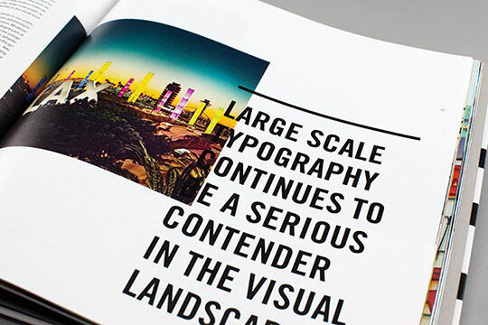 Open magazine with a colorful cityscape and large bold text on the right page reading, "Large Scale Typography Continues to Be a Serious Contender in the Visual Landscape."